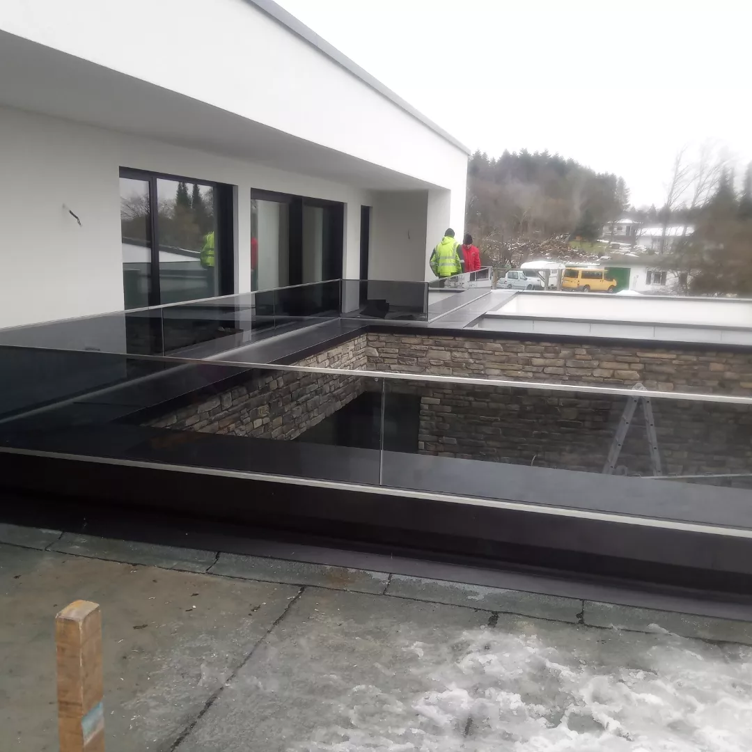 Rahmenloses Ganzglasgeländer an einer Dachterrasse mit Natursteinwand